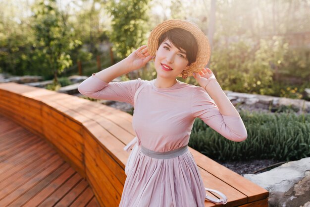 Graceful young lady in vintage clothes gladly posing in park enjoying sunlight