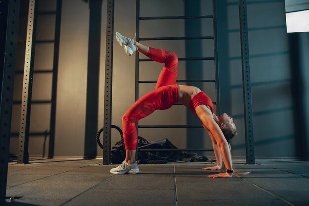 Graceful. Young muscular caucasian woman practicing in gym. Athletic female model doing strength exercises, training her lower, upper body, stretching. Wellness, healthy lifestyle, bodybuilding.