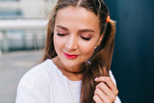 Graceful young woman with shiny hair gladly walks outside in good mood