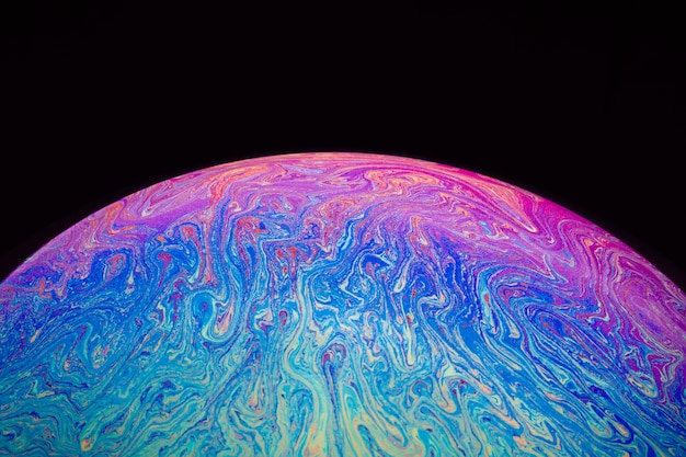 Gradient hued rippled soap bubble on black background