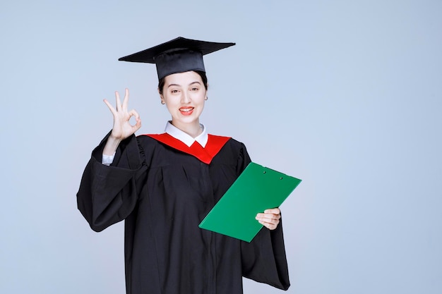 Graduate student with diploma holding alarm clock for showing time. High quality photo