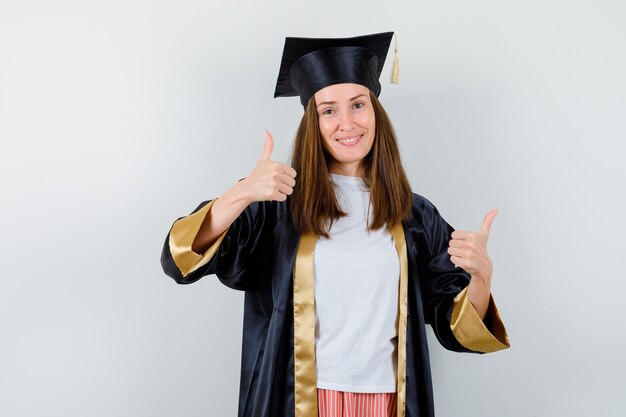 Женщина-выпускница показывает двойные пальцы вверх в повседневной одежде, униформе и выглядит уверенно. передний план.