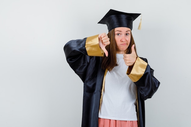 Graduate woman showing thumbs up and down in casual clothes, uniform and looking indecisive. front view.