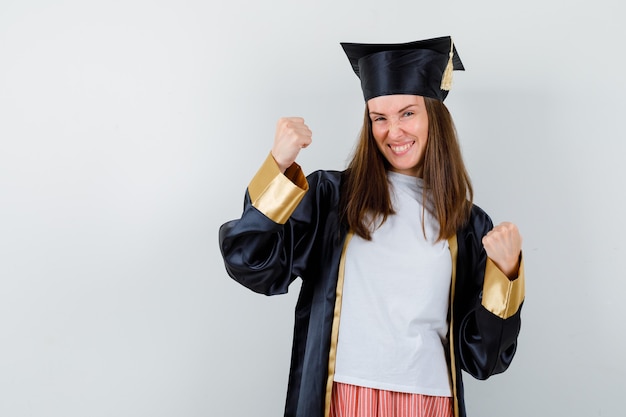 カジュアルな服装で勝者のジェスチャーを示す大学院の女性、制服を着て、至福のように見える、正面図。