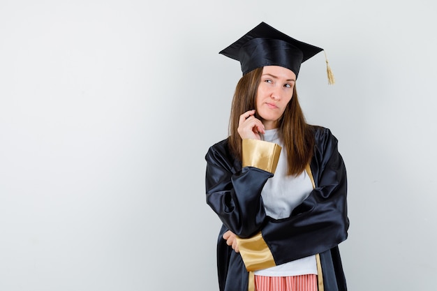 Graduate woman standing in thinking pose, curving lips in casual clothes, uniform and looking hesitant , front view.