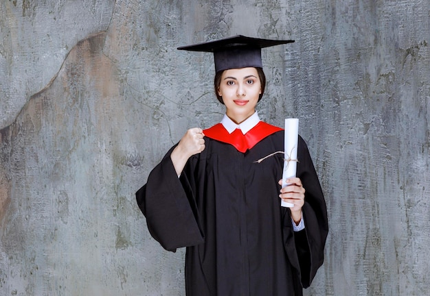 Graduated young woman in gown posing with university diploma. High quality photo