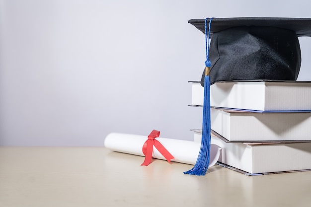 白い​backgrou​に対して​テーブル​の​上​の​本​と​卒業​証書​と​卒業​の​帽子
