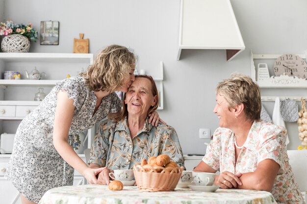 Внучка целует свою улыбающуюся бабушку во время завтрака
