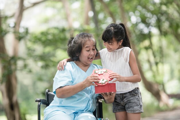 Внучка удивляет бабушку, сидящую на инвалидной коляске.