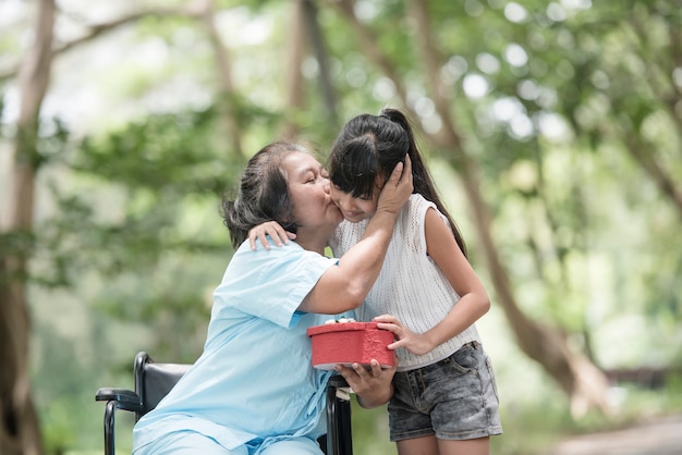 Granddaughter have surprise to grandmother sitting on wheelchair.