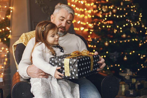 Grandfather sitting with his granddaughter. Celebrating Christmas in a cozy house. Man in a white knited sweater.