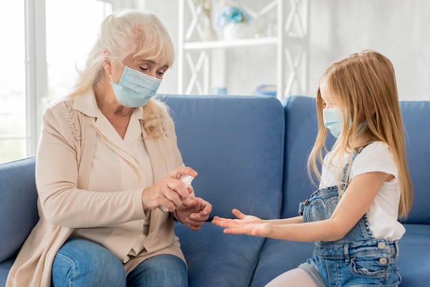 Nonna e ragazza con maschera usando disinfettante per le mani