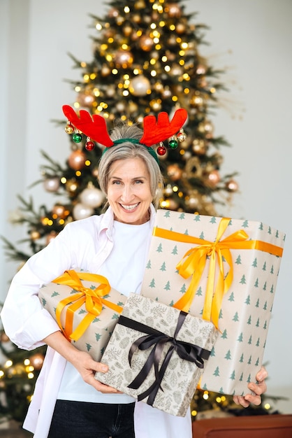 Бабушка в оленьей рождественской шапке рождественские подарки в руках