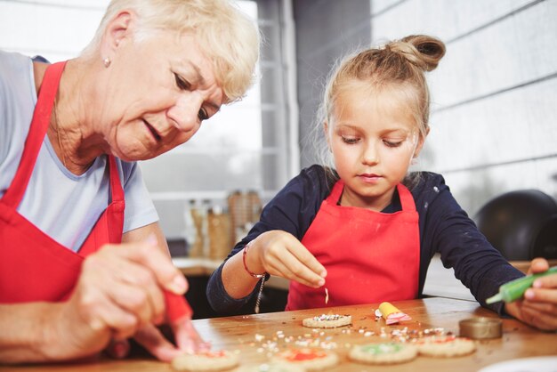 Grandma with girl applying icing on cookies