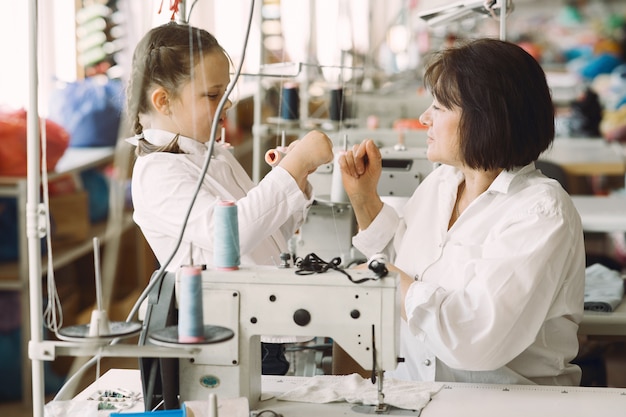 Grandma with little granddaughter sew clothes in the factory