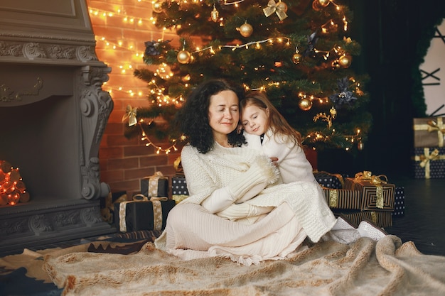 Grandmother sitting with her granddaughter. Celebrating Christmas in a cozy house. Woman in a white knited sweater.