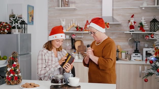 Grandmother surprising grandchild with xmas wrapper gift present celebrating christmastime