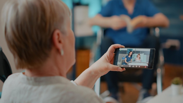 Grandmother using online conference call to chat with relatives on mobile phone. Retired adult talking on remote videoconference with daughter and niece, doing telecommunication.