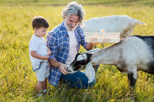 Grandpa and little boy feeding goat