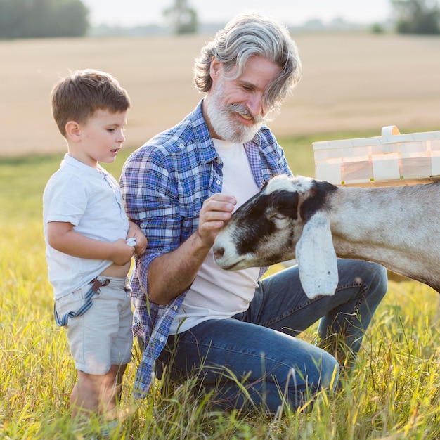 Foto gratuita nonno e ragazzino che giocano con le capre