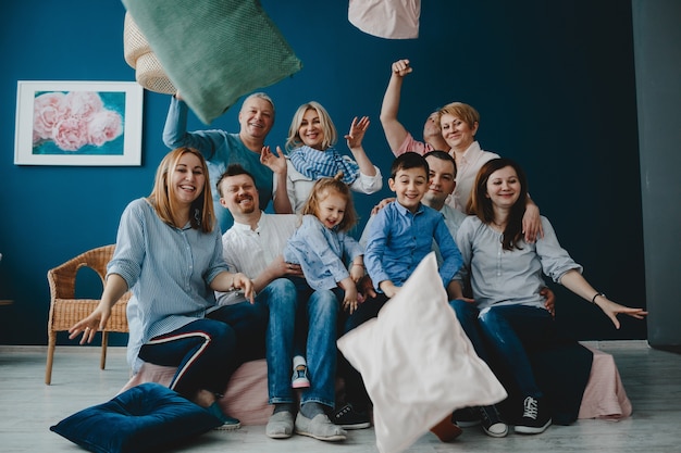 Grandparents, parents and their little children sit together on the bed in a blue room