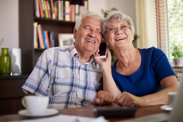 Бабушка и дедушка разговаривают по телефону за столом