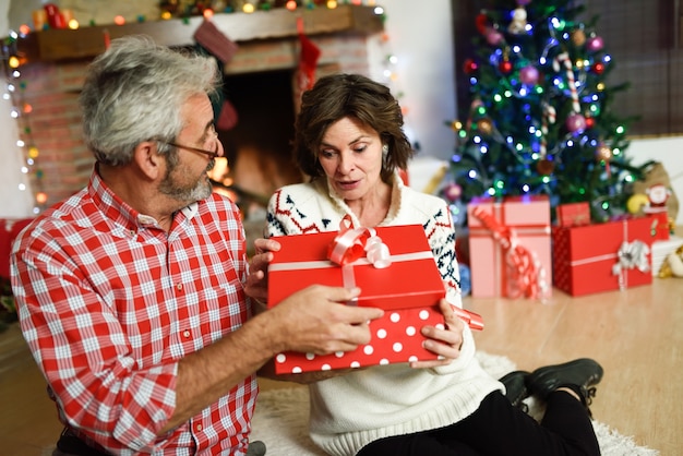 Бабушки и дедушки с подарочной совмещены коробки в их гостиной украшены к Рождеству