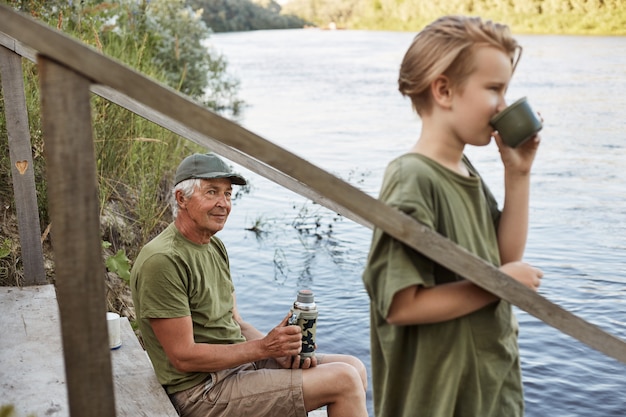 Внук и дедушка ловят рыбу на реке