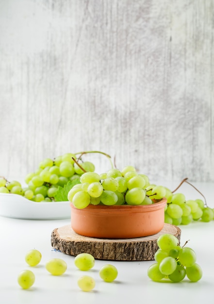 Grape clusters in plates with wooden piece side view on white surface