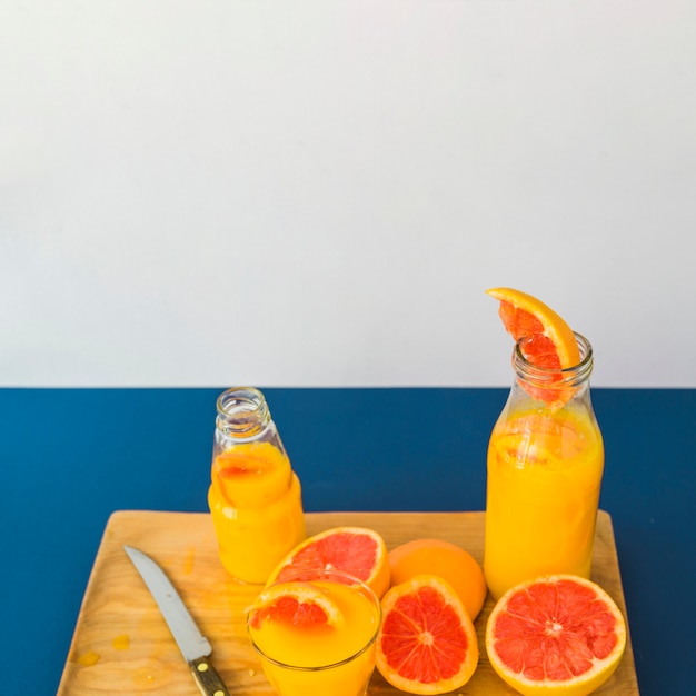 Grapefruit juice in bottle and glass on chopping board against blue background