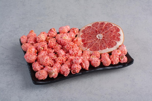 Grapefruit slice next to a serving of red popcorn candy on marble surface