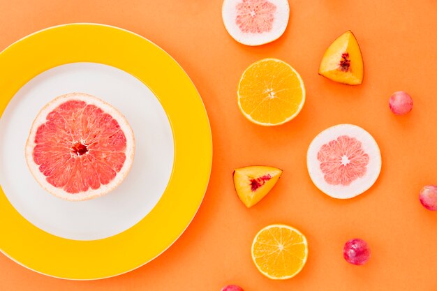 Grapefruit slice on white and yellow plate with fruits on an orange backdrop