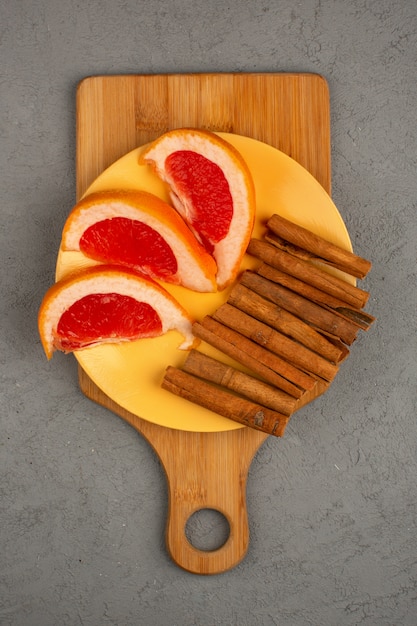 Свежие сочные кусочки грейпфрута внутри желтой пластины вместе с корицей на сером столе