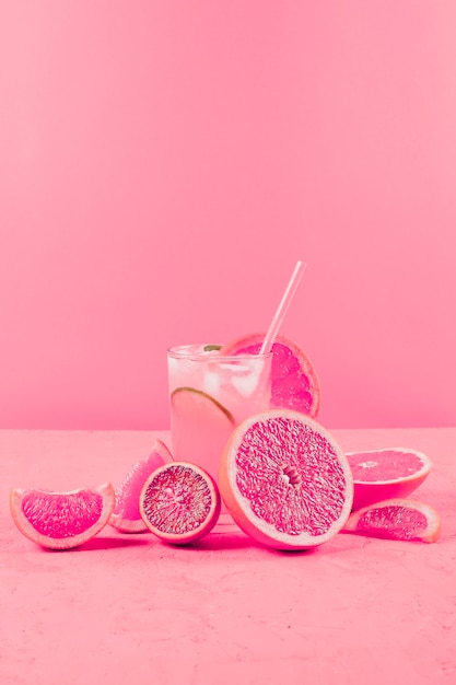 Grapefruit slices and glass of juice on pink textured backdrop