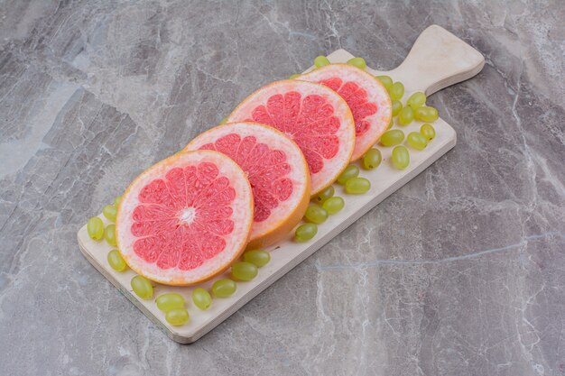 Grapefruit slices and grapes on wooden board. 