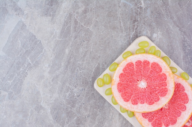 Grapefruit slices and green grapes on wooden board. 