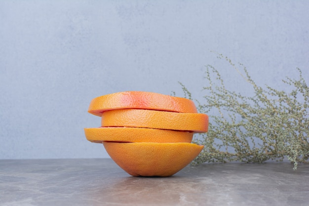 Grapefruit slices on stone table with plant. 