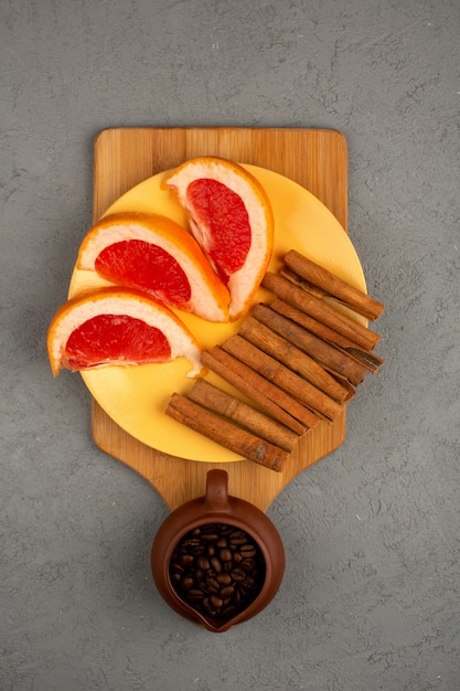 Free photo grapefruit slices with cinnamon and brown coffee seeds inside pot on a grey floor