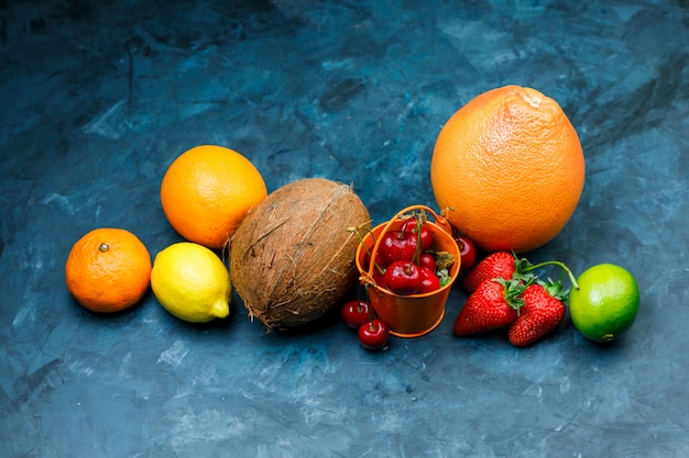 Free photo grapefruit with orange, lime, lemon, strawberry, cherry, tangerine, coconut flat lay on a grungy blue surface