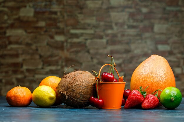 벽돌 돌과 파란색 배경에 오렌지, 라임, 레몬, 딸기, 체리, 귤, 코코넛 측면보기 자몽