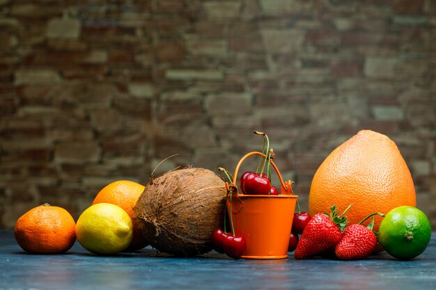 Grapefruit with orange, lime, lemon, strawberry, cherry, tangerine, coconut side view on brick stone and blue background