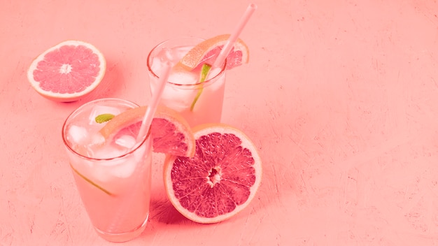 Grapefruits cocktail with fruit slices and ice cubes on coral textured background