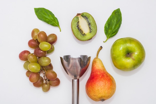 Grapes; basil; kiwi; apple and pear with electric hand blender on white background