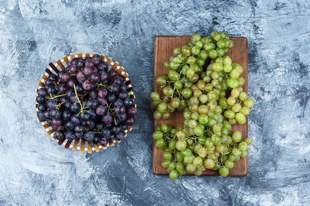 Free photo grapes in a basket flat lay on grungy plaster and cutting board background