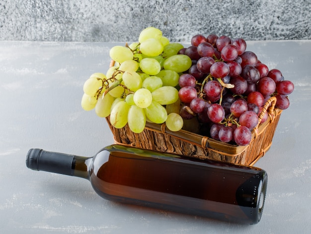 Виноград в корзине с бутылкой для питья под высоким углом зрения на гипсе и шероховатый
