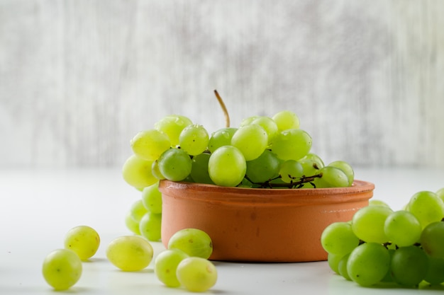 Grapes in a clay plate on white surface, side view.