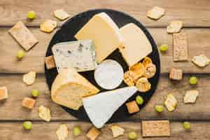 Free photo grapes, cracker, crisp bread and cheese blocks on round slate over the wooden desk