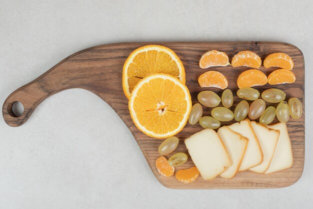 Grapes, oranges, tangerines and cheese on wooden board