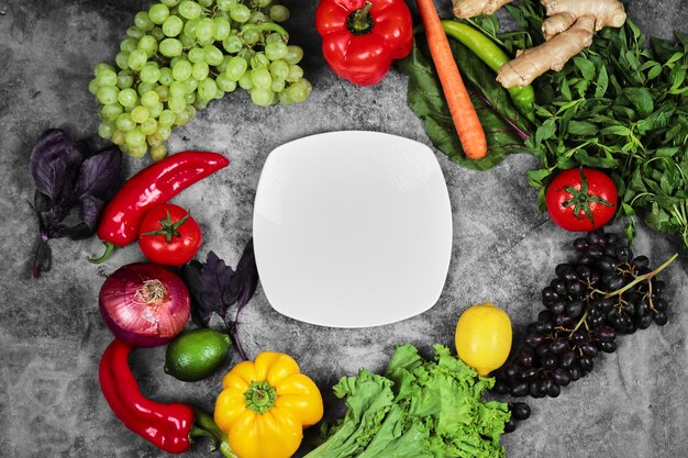 Grapes, peppers, greens, lemon, tomato , ginger and white plate on marble background. 