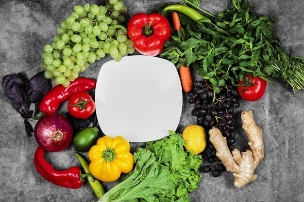 Grapes, peppers, greens, lemon, tomato , ginger and white plate on marble background. 